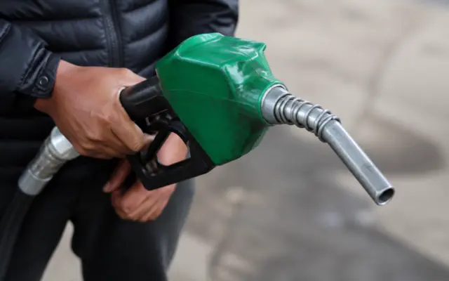 A person holding a green fuel nozzle at a gas station, symbolizing diesel fuel consumption