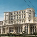 O fotografie de ansamblu a Palatului Parlamentului din București, clădire masivă cu arhitectură neoclasică, sub un cer senin