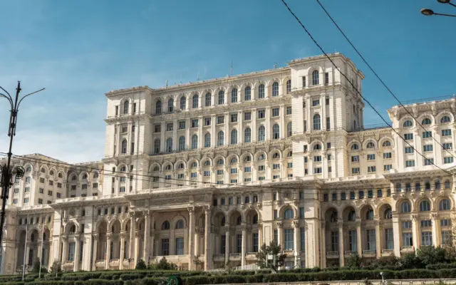 O fotografie de ansamblu a Palatului Parlamentului din București, clădire masivă cu arhitectură neoclasică, sub un cer senin