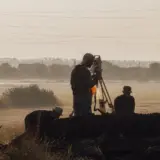 Surveyors using a total station on a tripod in a misty field for land measurement