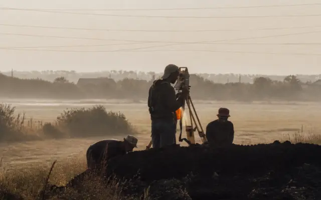 Surveyors using a total station on a tripod in a misty field for land measurement