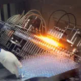 O mașină industrială complexă într-un proces de fabricație, cu flăcări care sigilează flacoane de sticlă pe o bandă rulantă