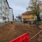 A construction site for a parking lot between residential buildings with excavators and red safety barriers