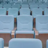 Rânduri succesive de scaune de culoare bleu, cu brațe din lemn, dintr-o sală de cinema sau amfiteatru