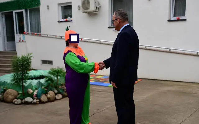 Man in suit shaking hands with a person in a colorful costume at a care center