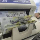 O mașină de numărat bani (aparat iSNIPER) prin care trec teancuri de bancnote de 100 de lei românești (RON), ilustrând fluxurile financiare și banii publici