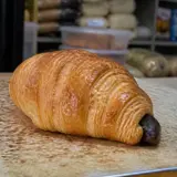 Un corn (croissant) cu ciocolată așezat pe o tejghea maronie, aspră